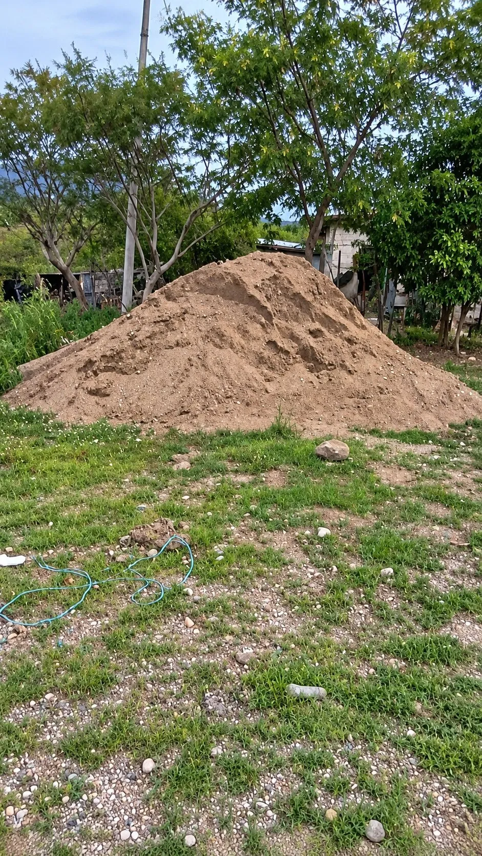 Un montón grande de arena en un terreno con pasto y árboles al fondo